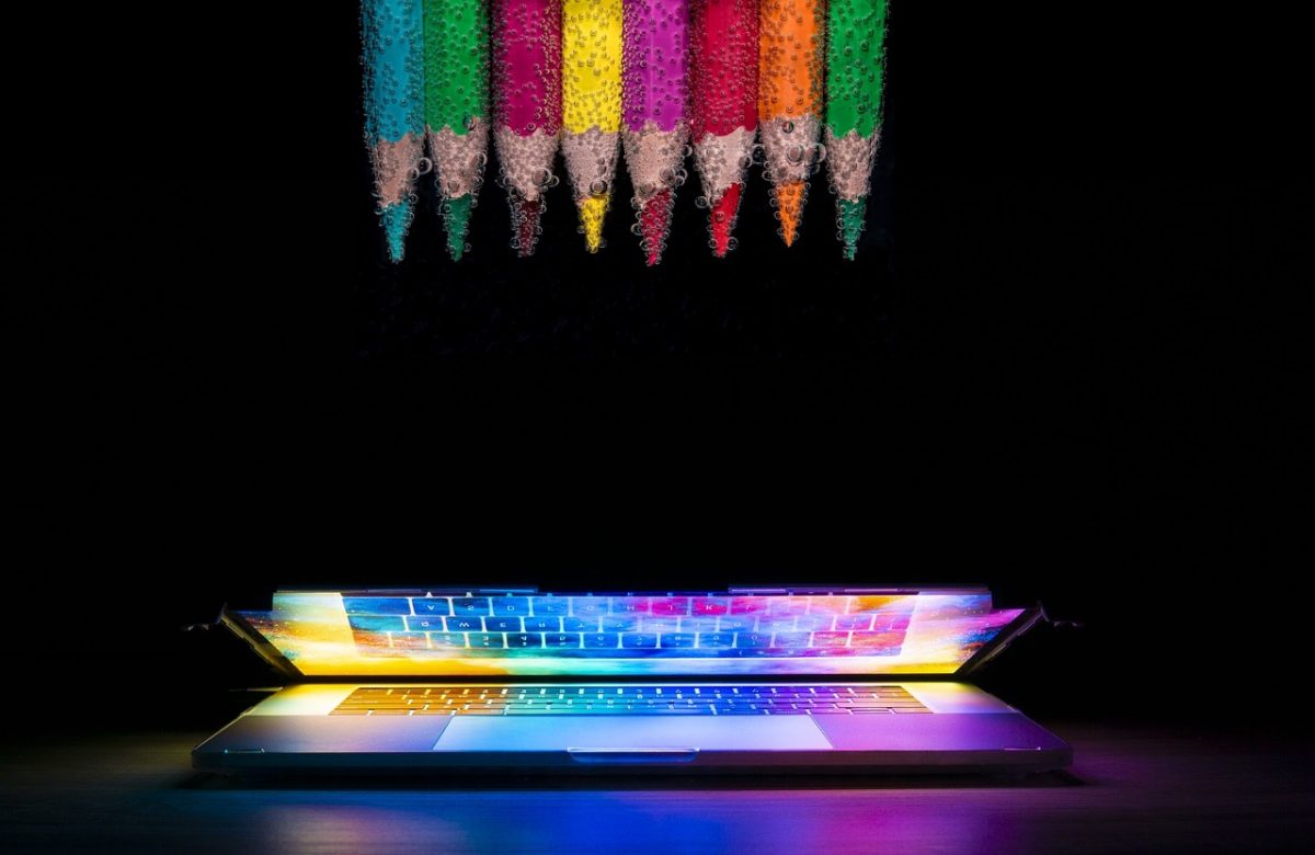 Laptop computer showing a colorful display. At the top are color pencils used for web front end design.